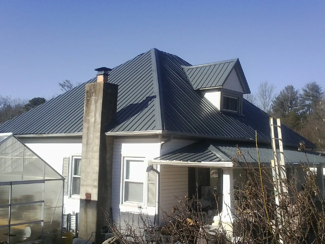 Dark blue standing seam metal roof on a white farmhouse with dormer — Slate & Tile Roof Repair by Roofing Brothers in Sugarloaf