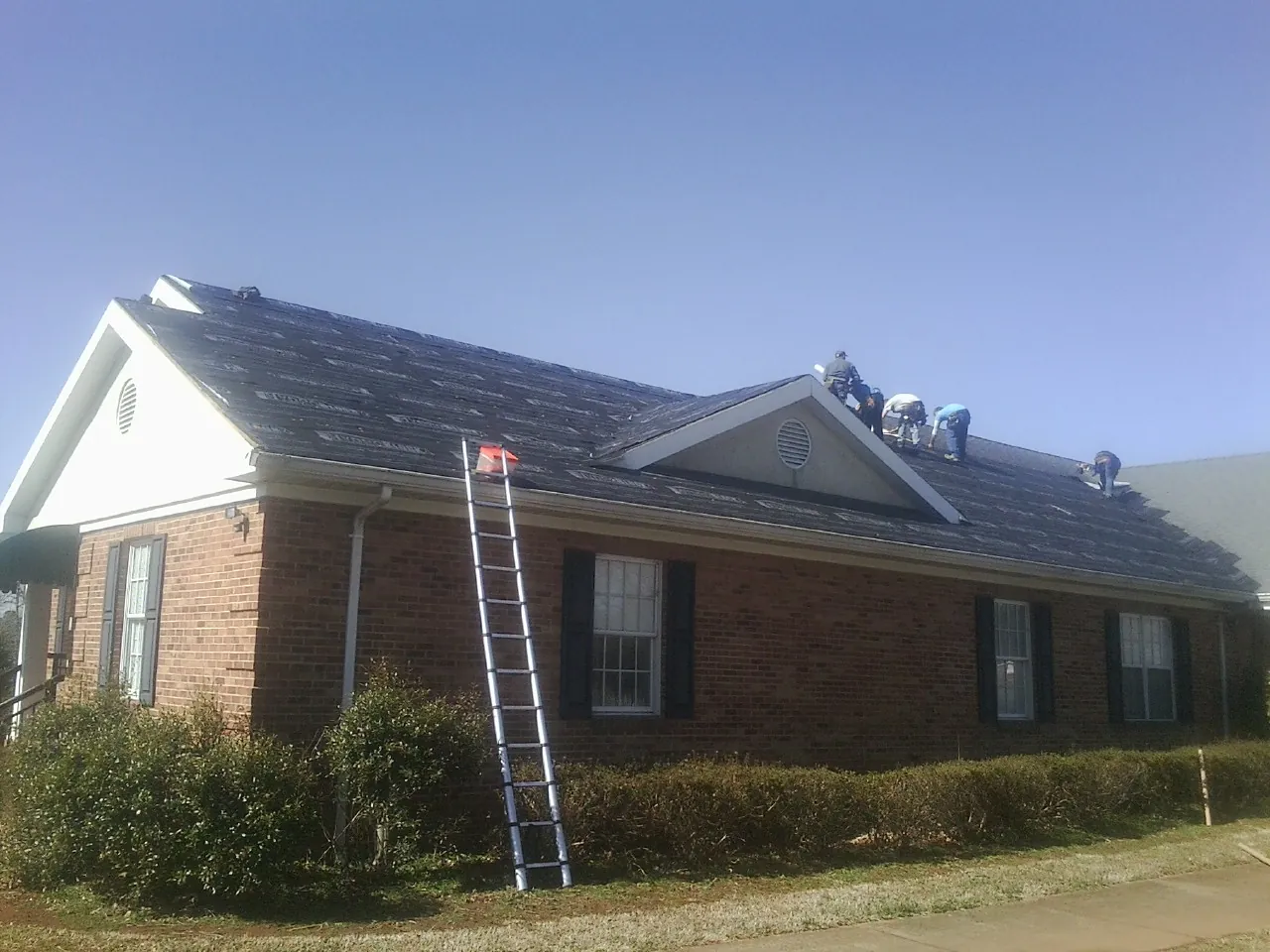 Crew tearing shingles off a brick ranch roof with a ladder set — Emergency Roof Repair work by our crew in Sugarloaf