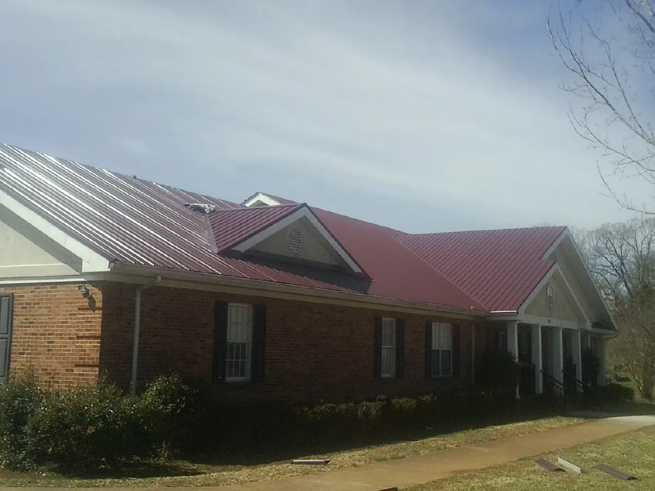 Red metal roof with gabled entries on a long brick building, from a Hail Damage Roof Repair job in Sugarloaf
