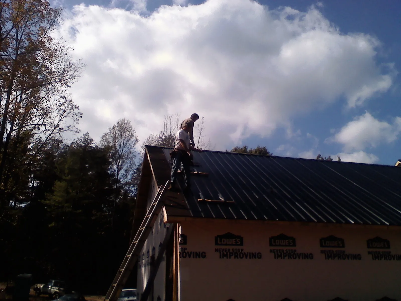 Roofer fastening dark metal panels high against a cloudy sky, from a Roof Inspection job in Sugarloaf