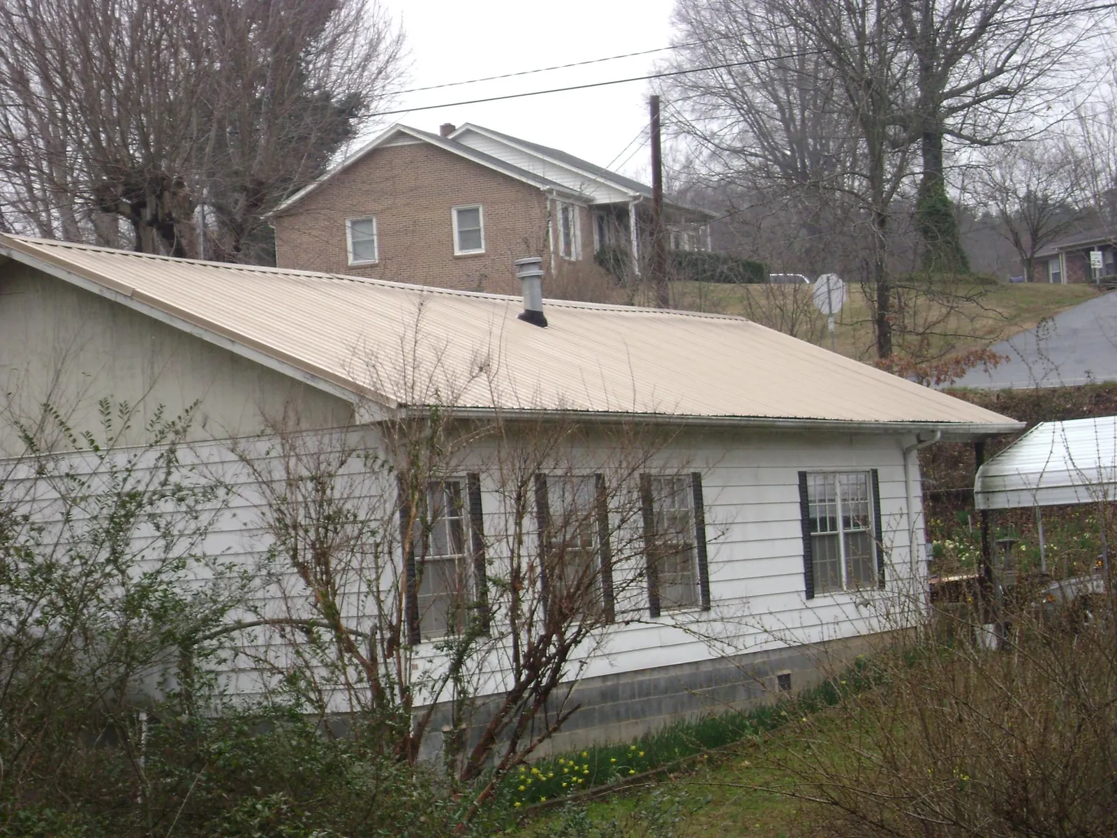 Tan metal roof on a white sided house set into a hillside — Commercial Roofing by Roofing Brothers in Sugarloaf